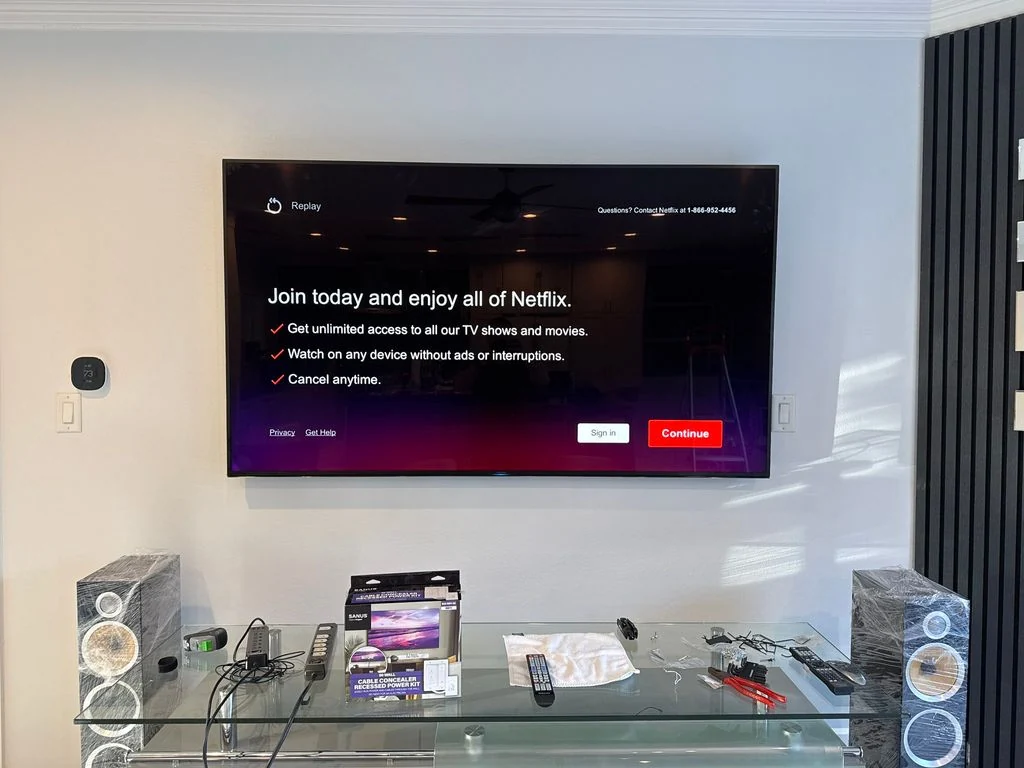 Wall-mounted television beside dark vertical wall panels during installation; tools and packaging remain below.